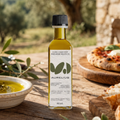 A bottle of Aurelius Early Harvest Premium Recycled Olive Oil stands on a rustic wooden table, surrounded by fresh olive branches, a bowl of oil with herbs, and a pizza on a wooden board in a warm, outdoor setting.